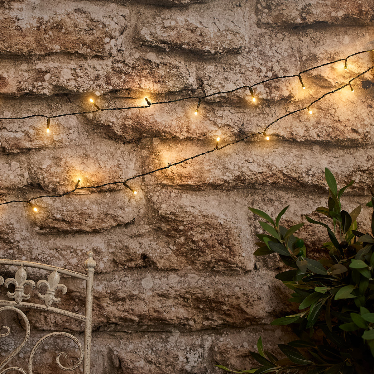 Solar Lichterkette mit warmweißen LEDs an Steinmauer und Pflanzen dekoriert
