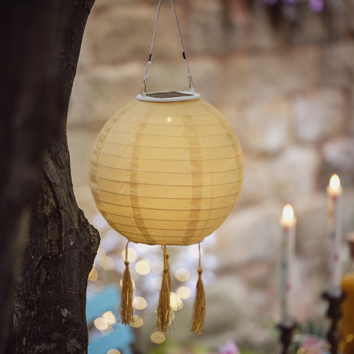 Nahaufnahme eines gelben Solar-Lampions mit Quasten an einem Baum im Garten