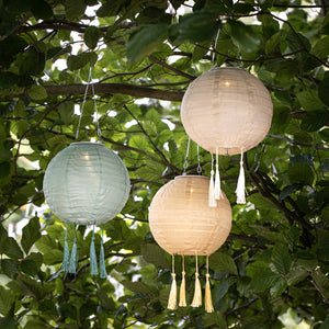 Drei Solar-Lampion in grün, gelb und crème hängen an einem Baumzweig