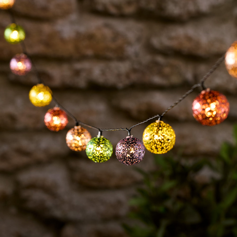 Bunte marokkanische Metallkugeln mit Lichtspiel an einer Lichterkette vor Steinwand
