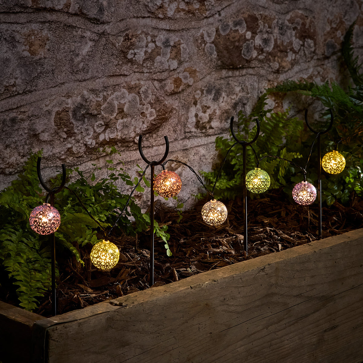 Solarbetriebene Lichterkette mit bunten Kugeln dekorativ in einem Beet mit Pflanzen