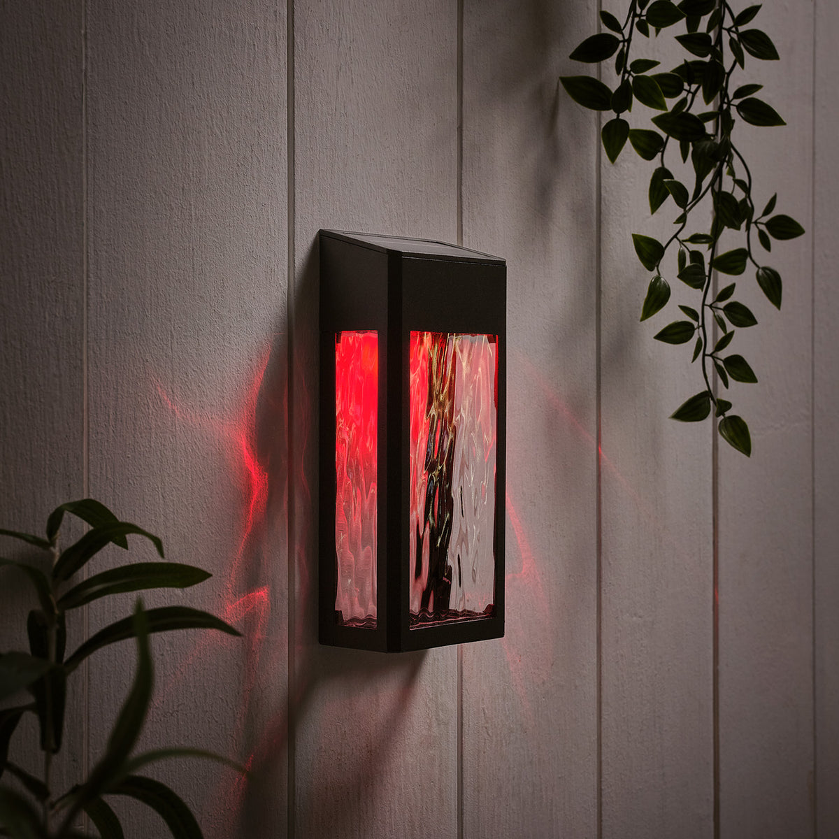 Solar-Wandleuchte mit rotem Licht an weißer Holzpaneelwand mit Pflanzenblättern