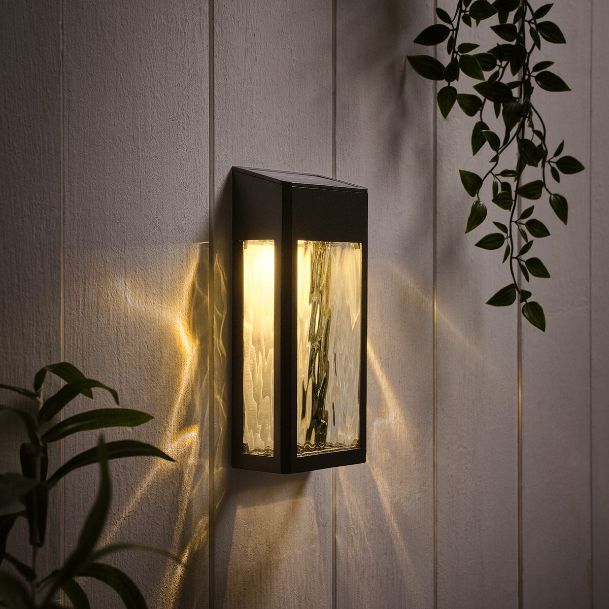 Schwarze Solar-Wandleuchte mit warmweißem Licht an weißer Holzpaneelwand