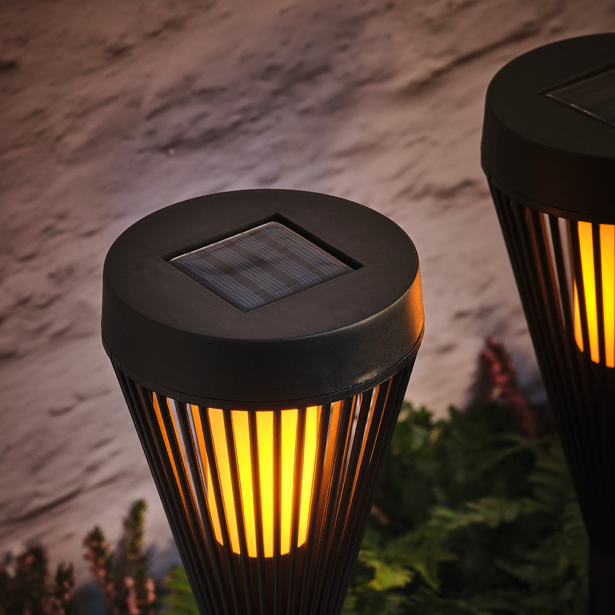 Nahaufnahme der Solar-Panel-Oberseite einer schwarzen Gartenfackel mit flackernder LED-Flamme