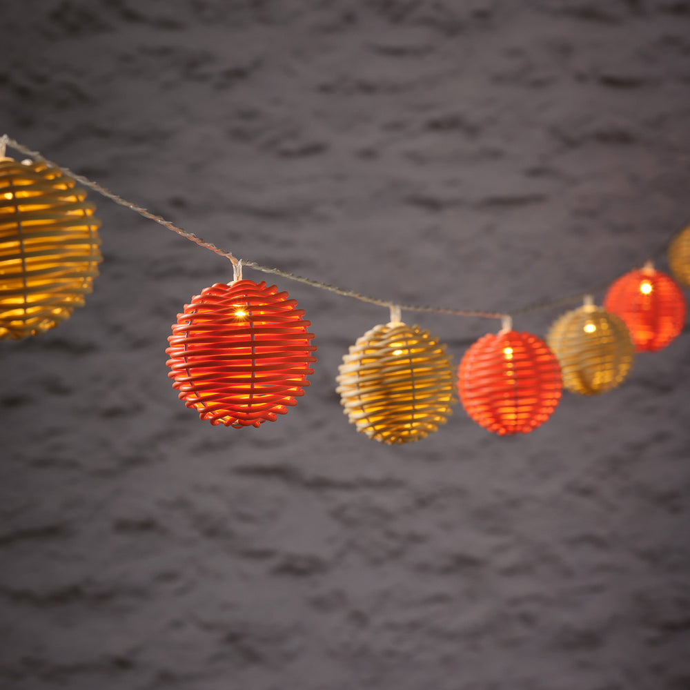 Nahaufnahme der leuchtenden Rattankugeln der LED Solar Lichterkette in Orange und Beige