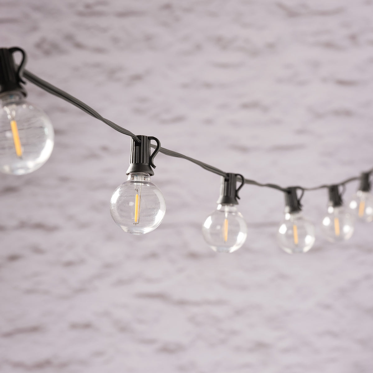 Solar-Lichterkette mit runden LED-Glühbirnen und schwarzem Kabel vor grauer Wand