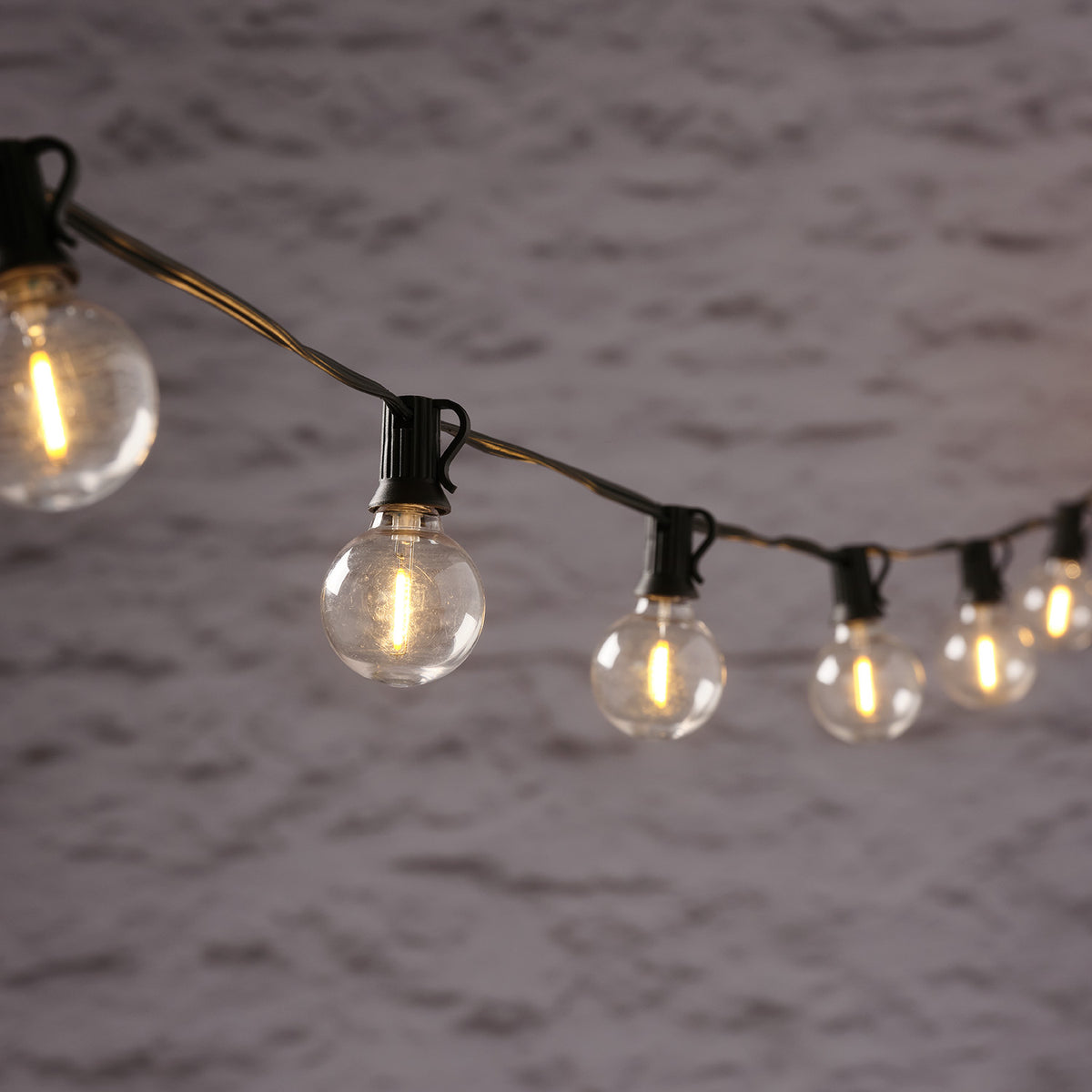 Solar-LED-Girlande mit klaren Glaskugeln und warmweißem Licht vor grauer Wand