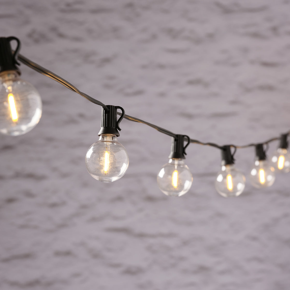 LED-Glühbirnen der Solar-Girlande hängen an schwarzem Kabel vor grauer Wand