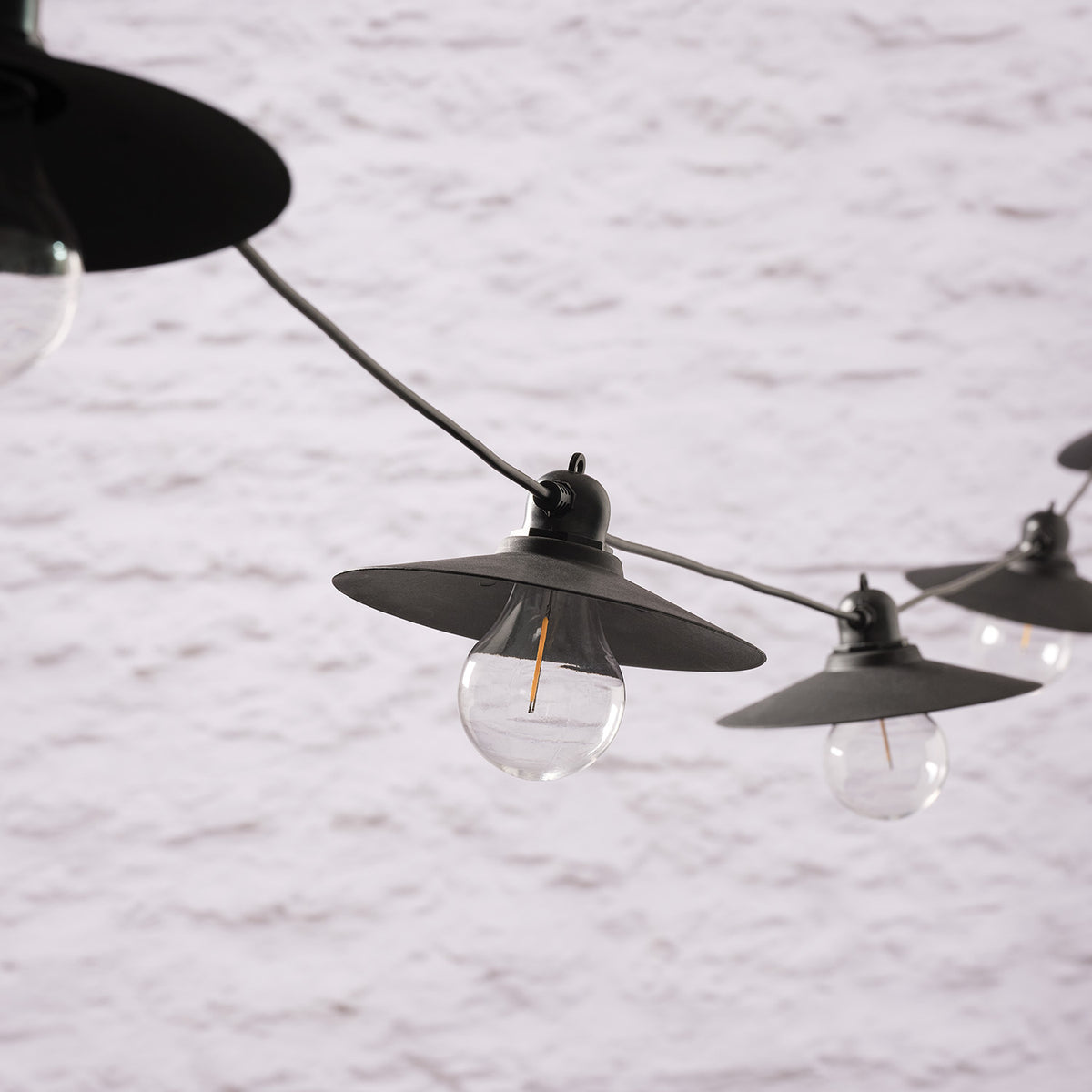 Unbeleuchtete LED-Glühbirnen mit schwarzen Lampenschirmen an schwarzem Kabel vor weißer Wand