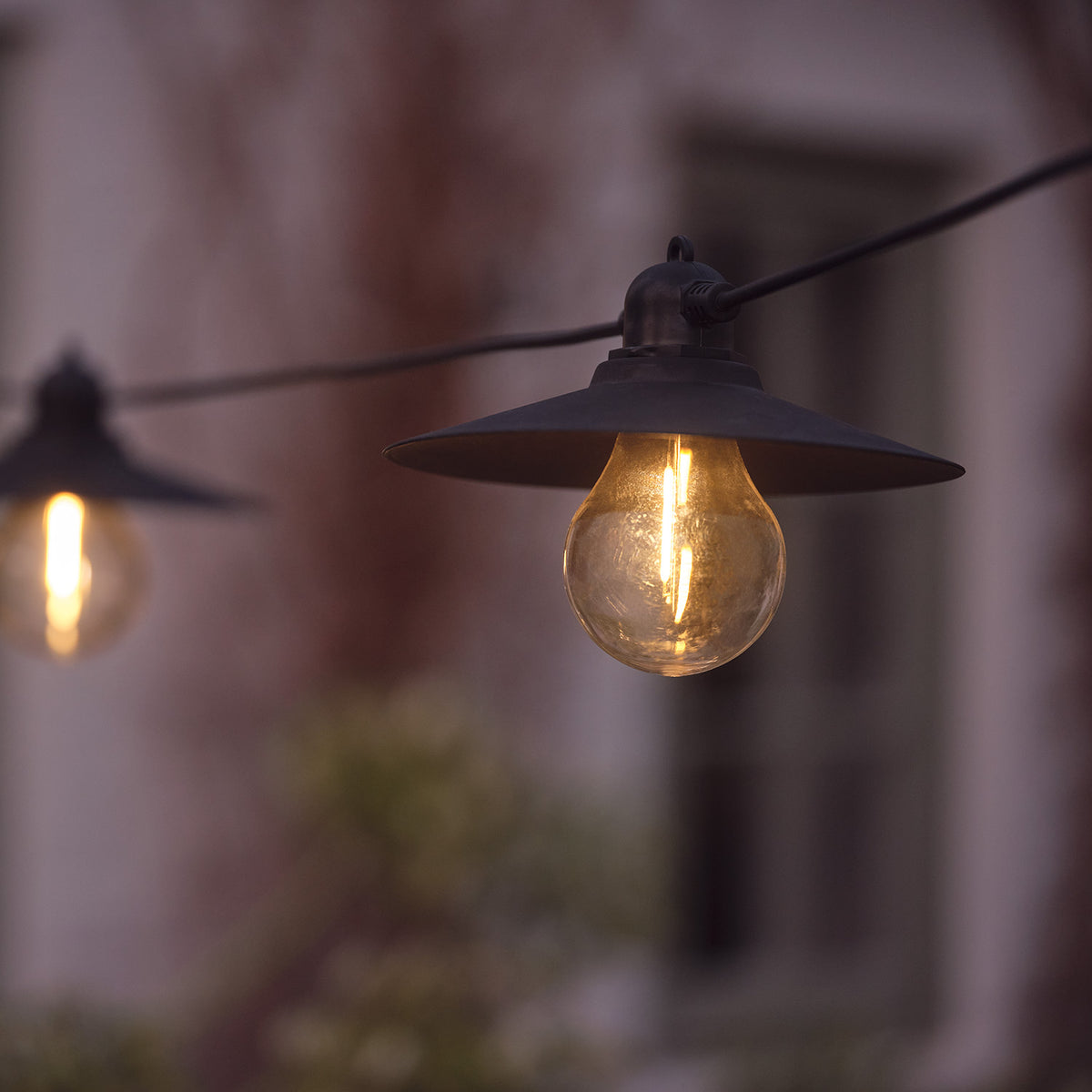 Nahaufnahme einer warmweißen LED-Glühbirne mit schwarzem Lampenschirm an solarbetriebener Lichterkette