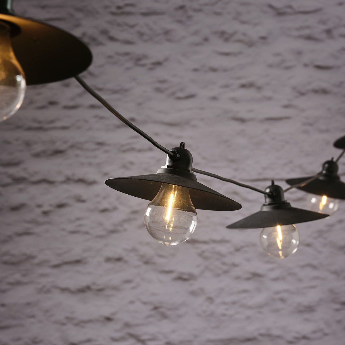 LED-Glühbirnen mit Retro-Lampenschirmen an schwarzer Lichterkette vor weißer Wand