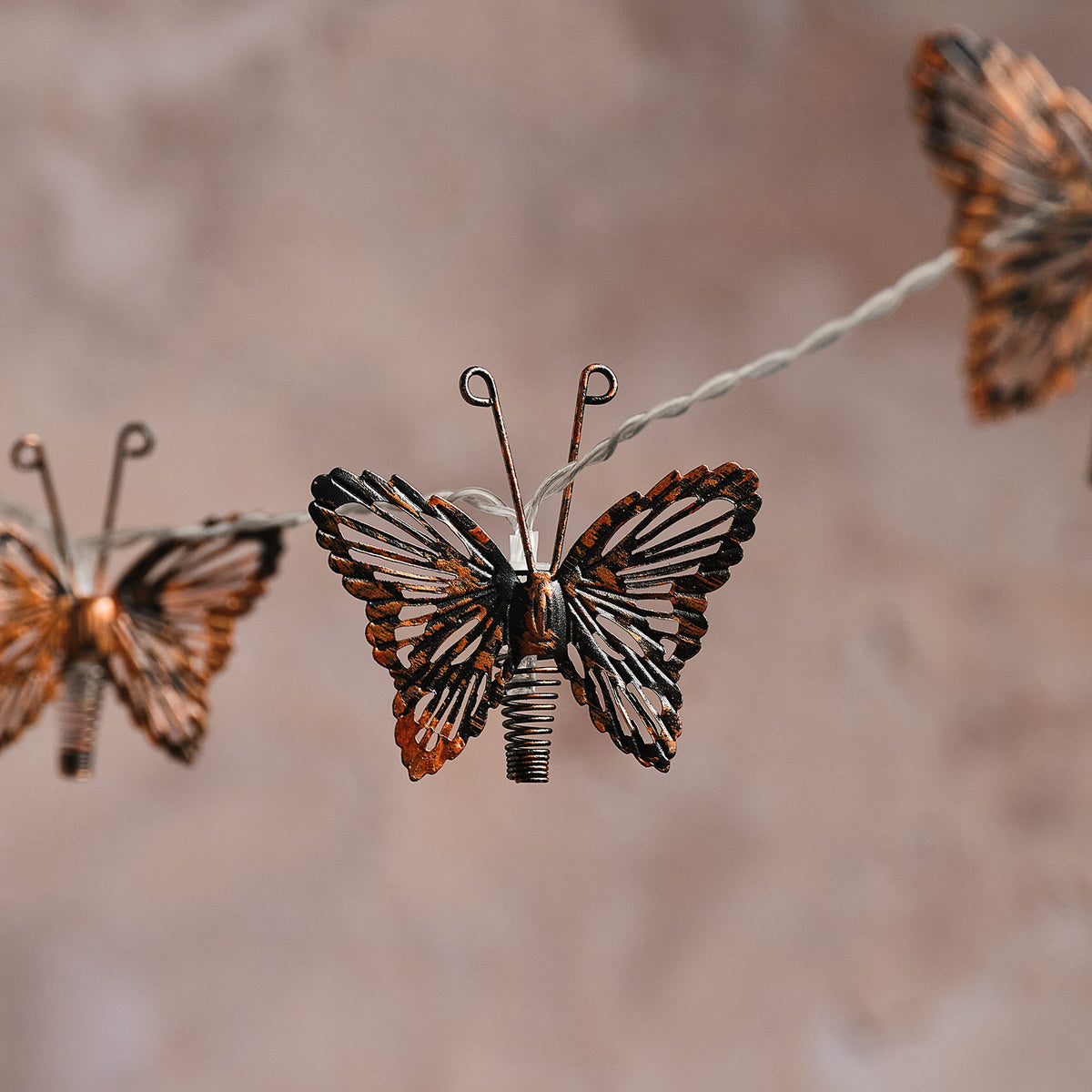 Kupferfarbener Metall-Schmetterling mit warmweißer LED auf Solar-Lichterkette vor hellem Hintergrund