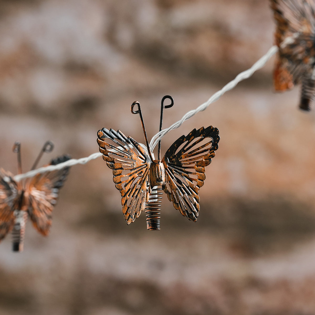 Kupferfarbener Metall-Schmetterling mit LED auf Solar-Lichterkette vor unscharfem Hintergrund