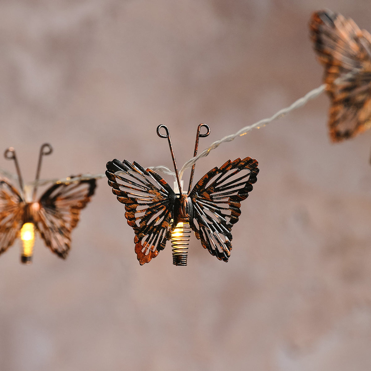 Detailaufnahme eines leuchtenden kupferfarbenen Metall-Schmetterlings auf Solar-Lichterkette