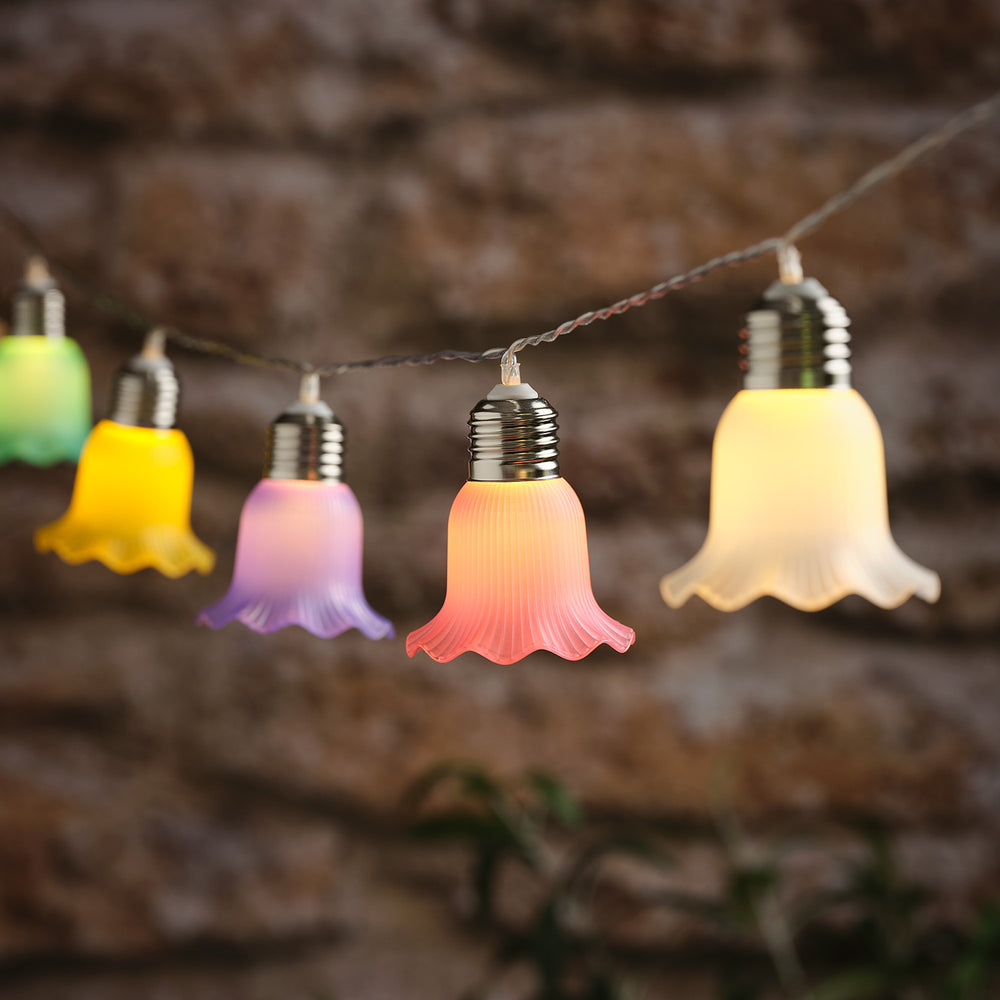 LED-Solar-Lichterkette mit pastellfarbenen Blumen in warmweiß leuchtend vor unscharfem Hintergrund