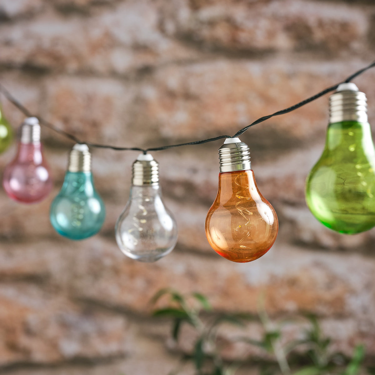 Solar-Lichterkette mit bunten Glühbirnen in Pastellfarben an schwarzem Kabel vor Steinwand
