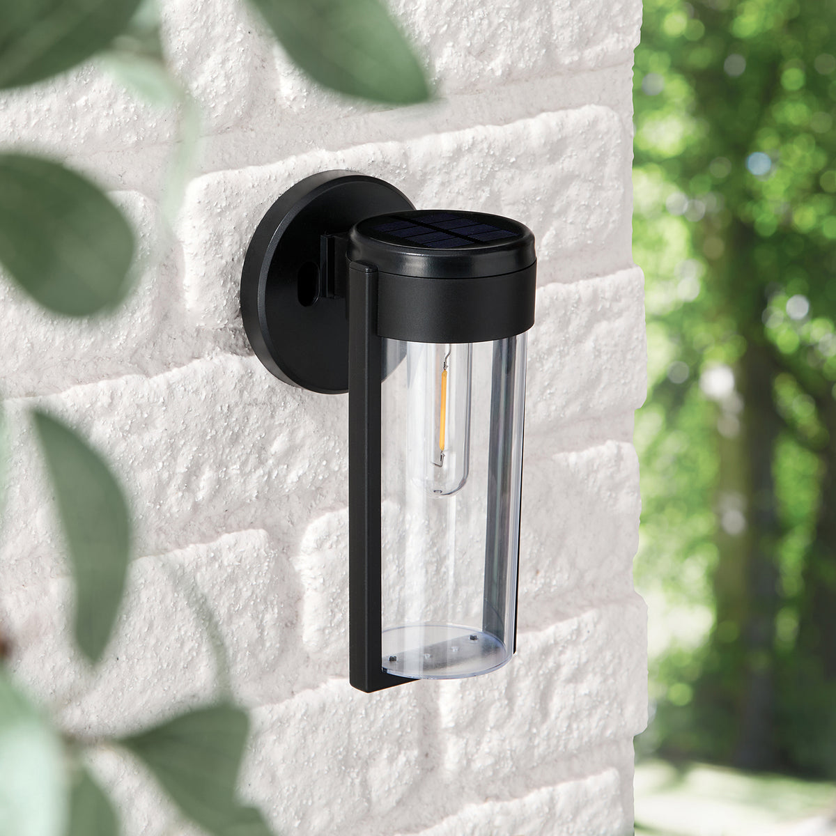 Schwarze Solar-Wandleuchte Wilton mit transparentem Zylinder an heller Steinwand bei Tageslicht