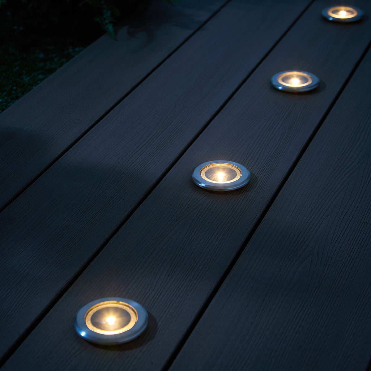 Solar-Einbaustrahler mit warmweißem Licht in dunklen Terrassendielen aus Holz
