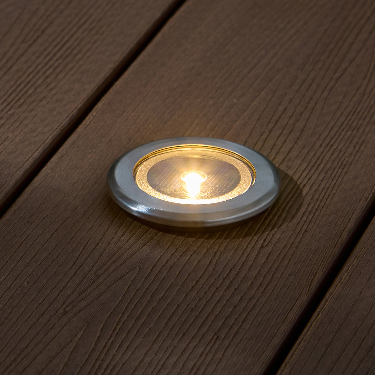 Nahaufnahme eines silbernen Solar-Terrassenstrahlers mit warmweißem LED-Licht in Holzterrasse