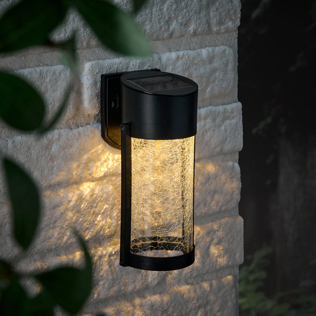 Solar-Wandleuchte mit Crackle-Glas leuchtet warmweiß an heller Steinwand bei Nacht
