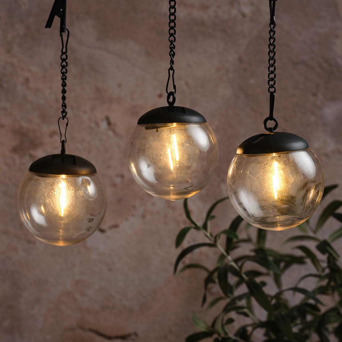 Drei transparente Solar-Hängelaternenkugeln mit warmweißem Filament-LED-Licht an schwarzen Ketten