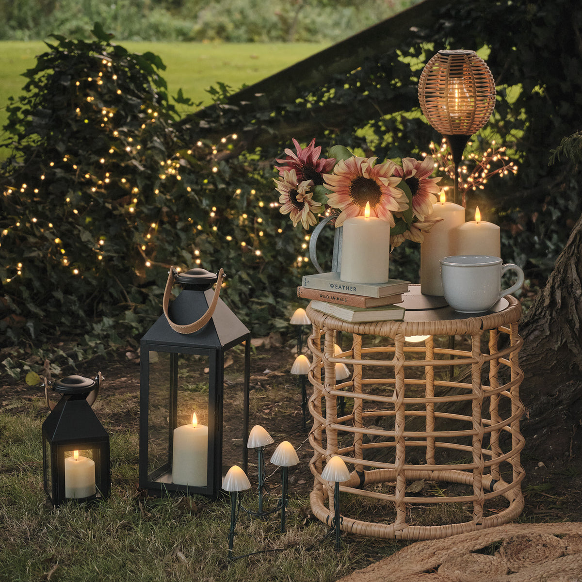 Solar-Beistelltisch in Flechtoptik mit Kerzen, Blumen und Tasse im Garten bei Dämmerung