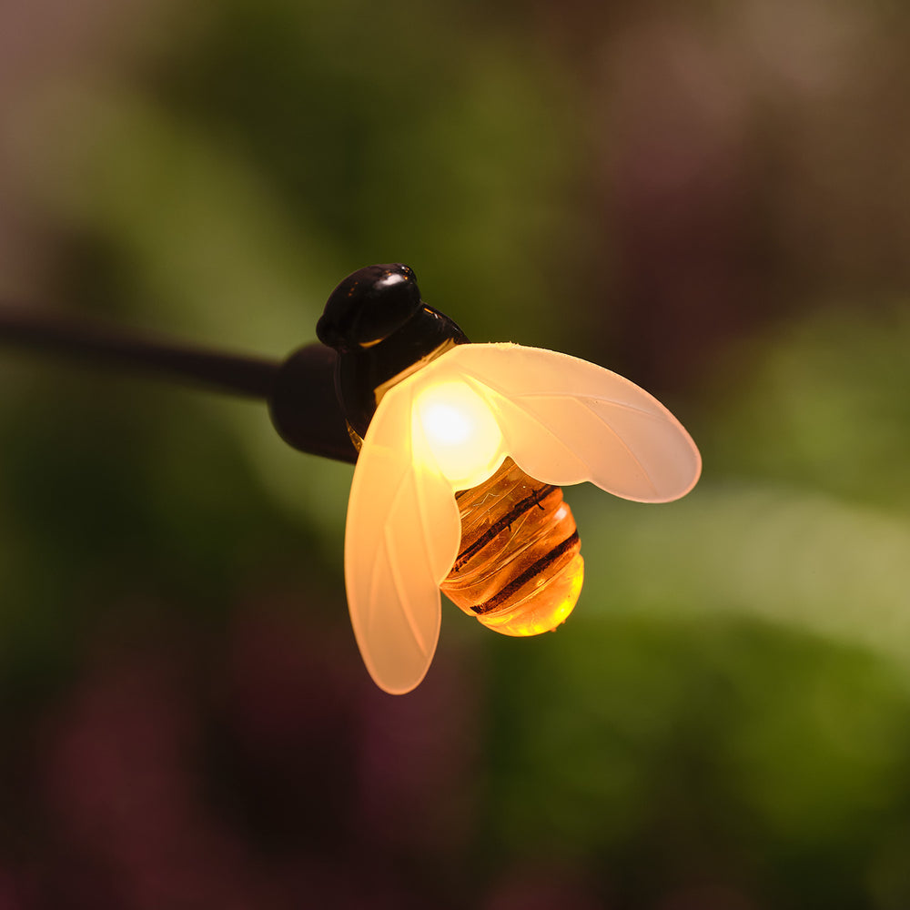 Nahaufnahme einer warmweiß leuchtenden Biene mit transparenten Flügeln am Solar-Gartenstecker