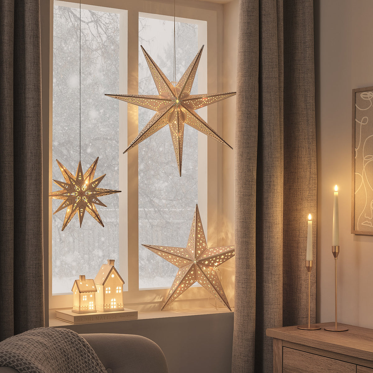 Drei verschiedene beleuchtete Holzsterne und Kerzen vor Fenster mit winterlicher Landschaft
