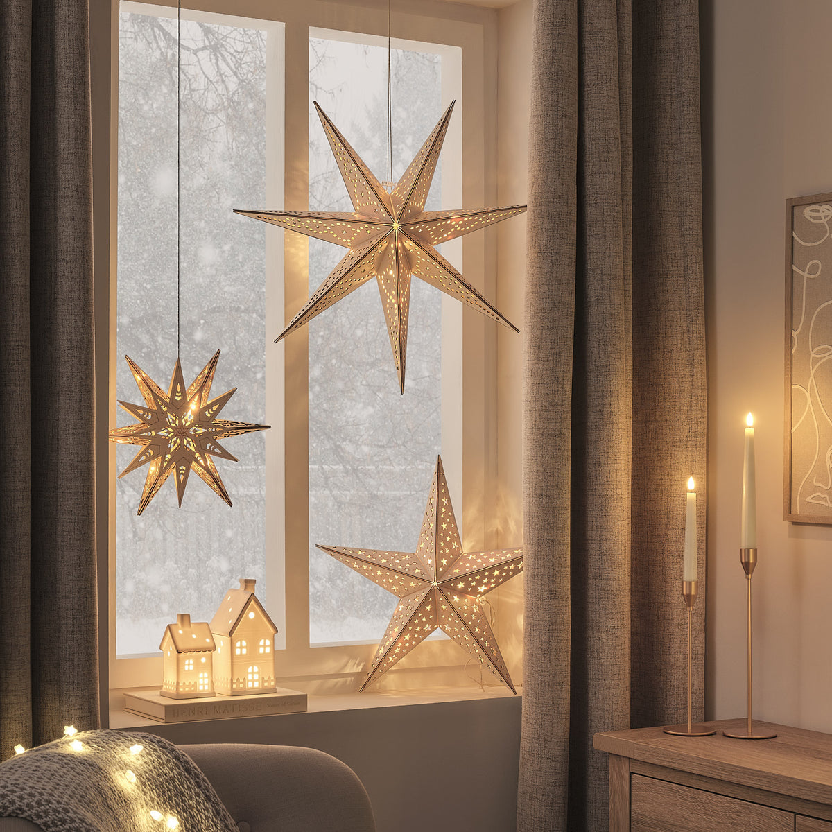 Drei beleuchtete Weihnachtssterne in Fensternische, warmweißes Licht, mit Vorhängen und Holzkommode