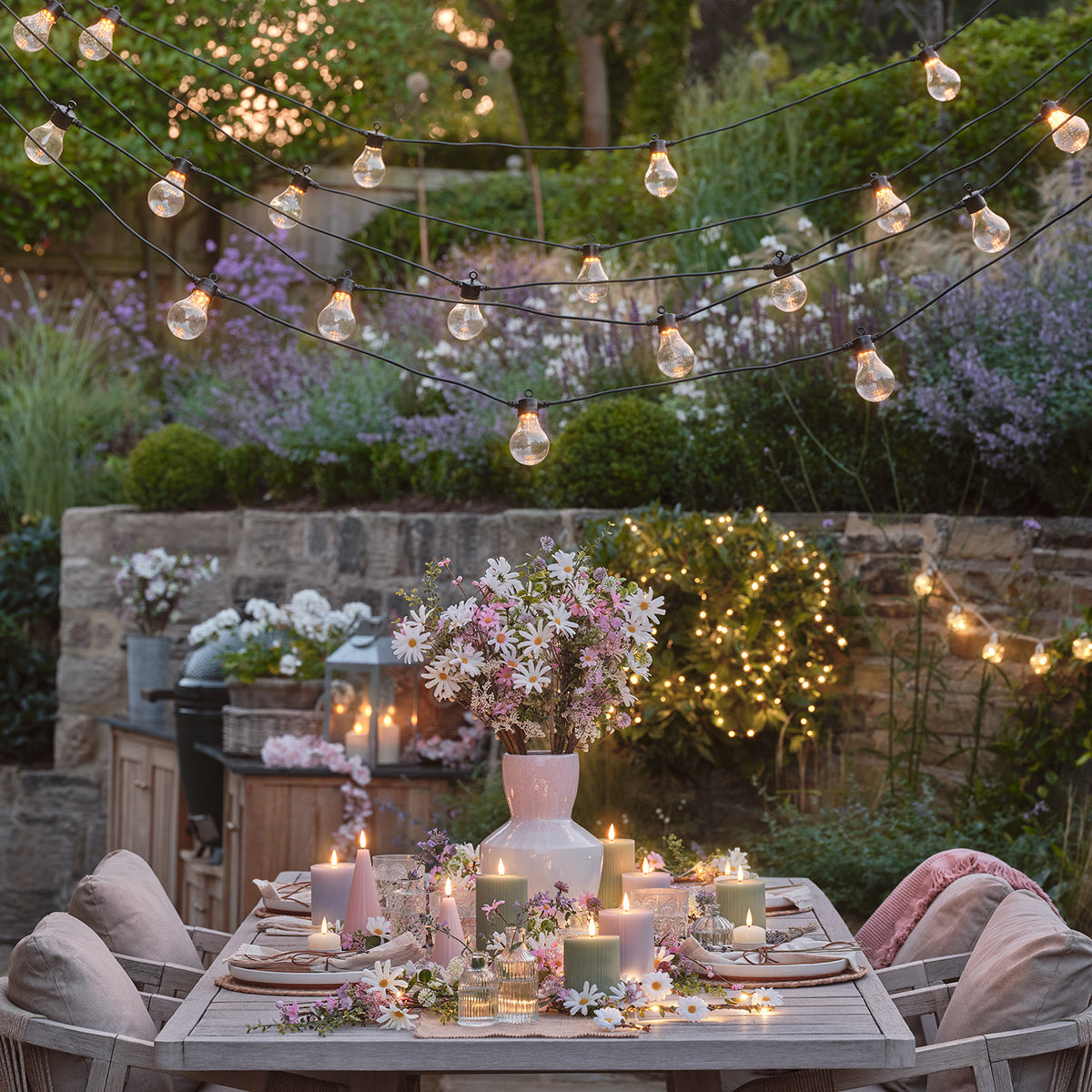 Romantisch gedeckter Gartentisch mit LED Blumengirlande, Kerzen und Blumenarrangement