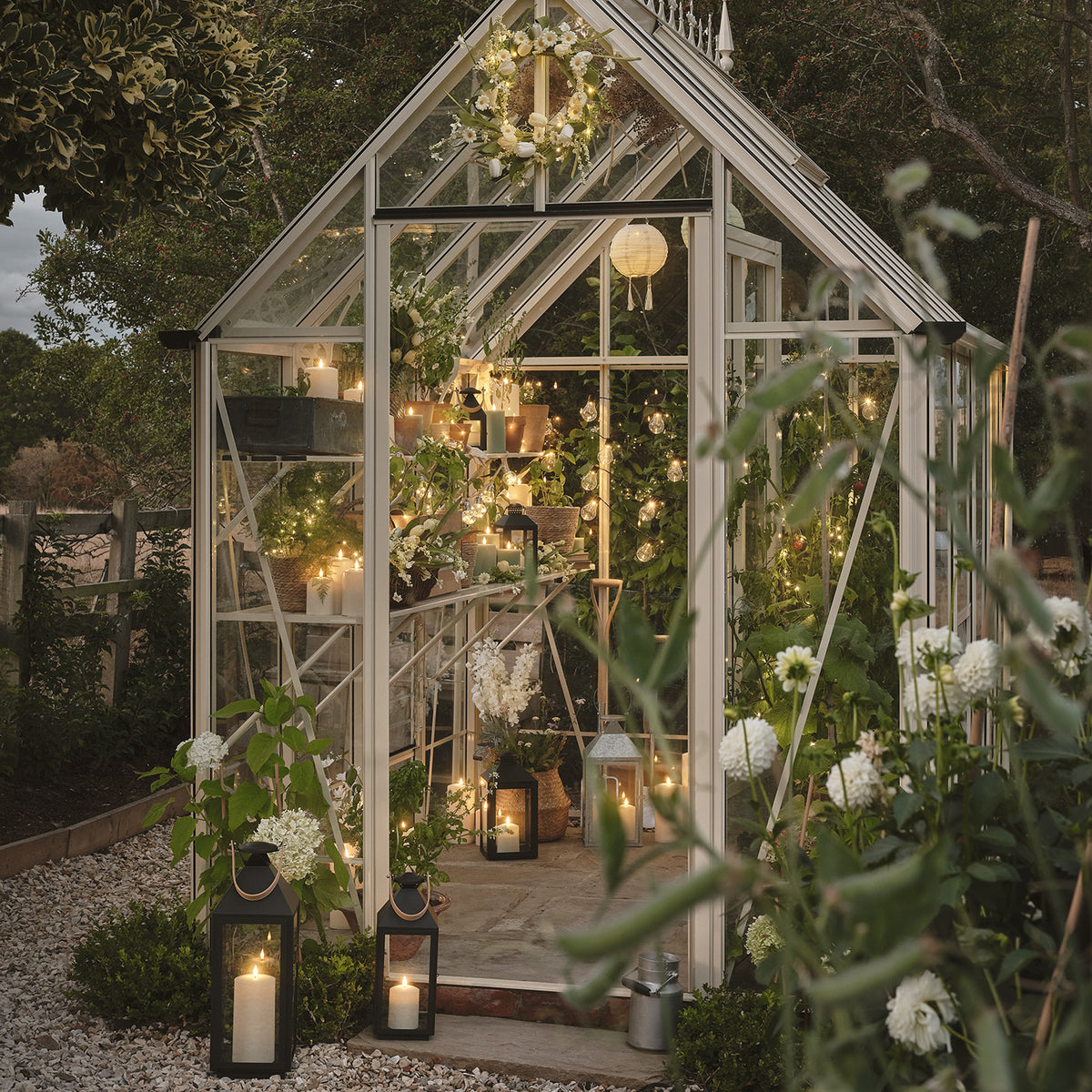 Gewächshaus mit Kerzen, Lichterketten und Frühlingskranz an der Außenseite im Garten