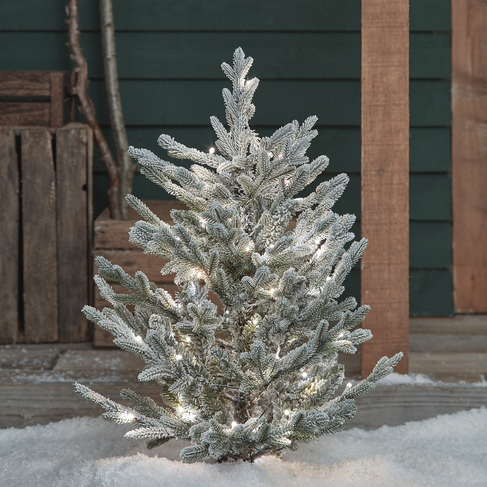 Verschneiter Weihnachtsbaum mit weißen LED-Lichtern im Schnee vor Holzverkleidung