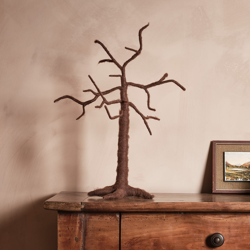Brauner Deko Baum aus Filz mit Metallgestell auf Holztisch vor beiger Wand