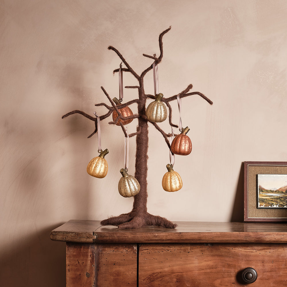 Filzbaum mit goldenen und kupferfarbenen Kürbisanhängern an den Ästen auf Holztisch