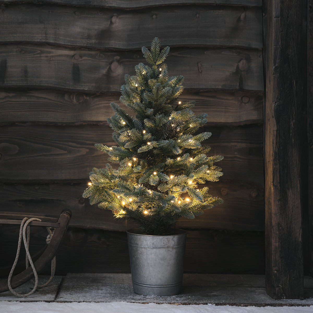 90cm hoher LED-Weihnachtsbaum im Metalltopf vor dunkler Holzwand mit warmweißen Lichtern