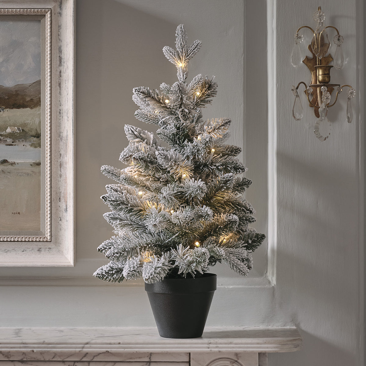 60 cm hoher verschneiter LED-Weihnachtsbaum in schwarzem Topf auf Marmorplatte vor grauer Wand