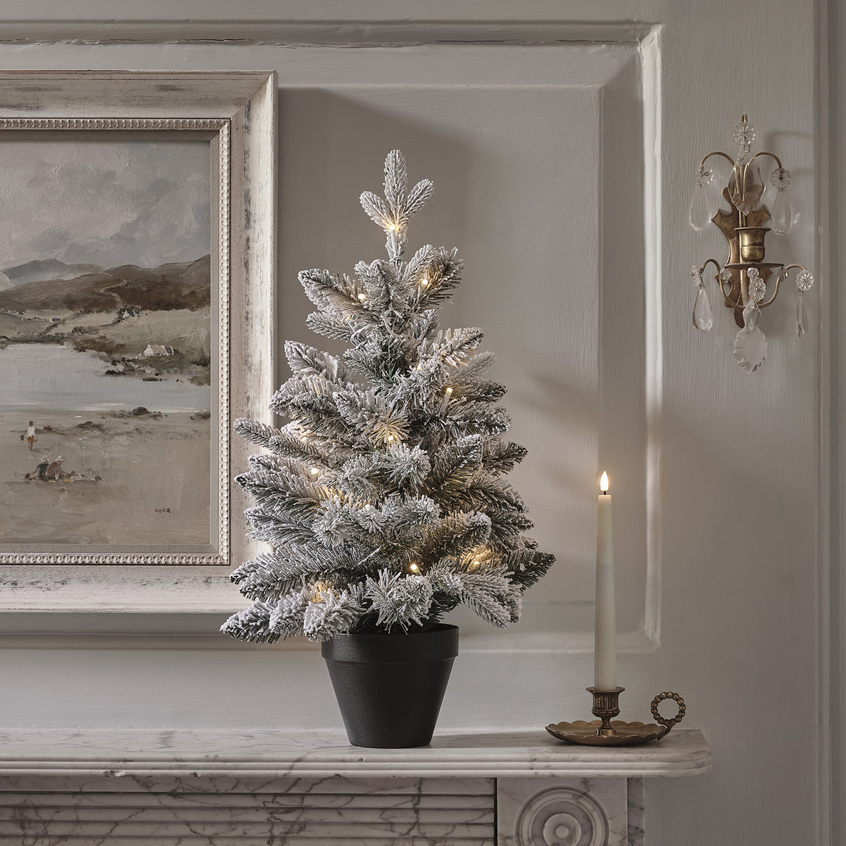 Verschneiter LED-Weihnachtsbaum mit warmweißen Lichtern auf Marmorplatte neben Kerzenhalter