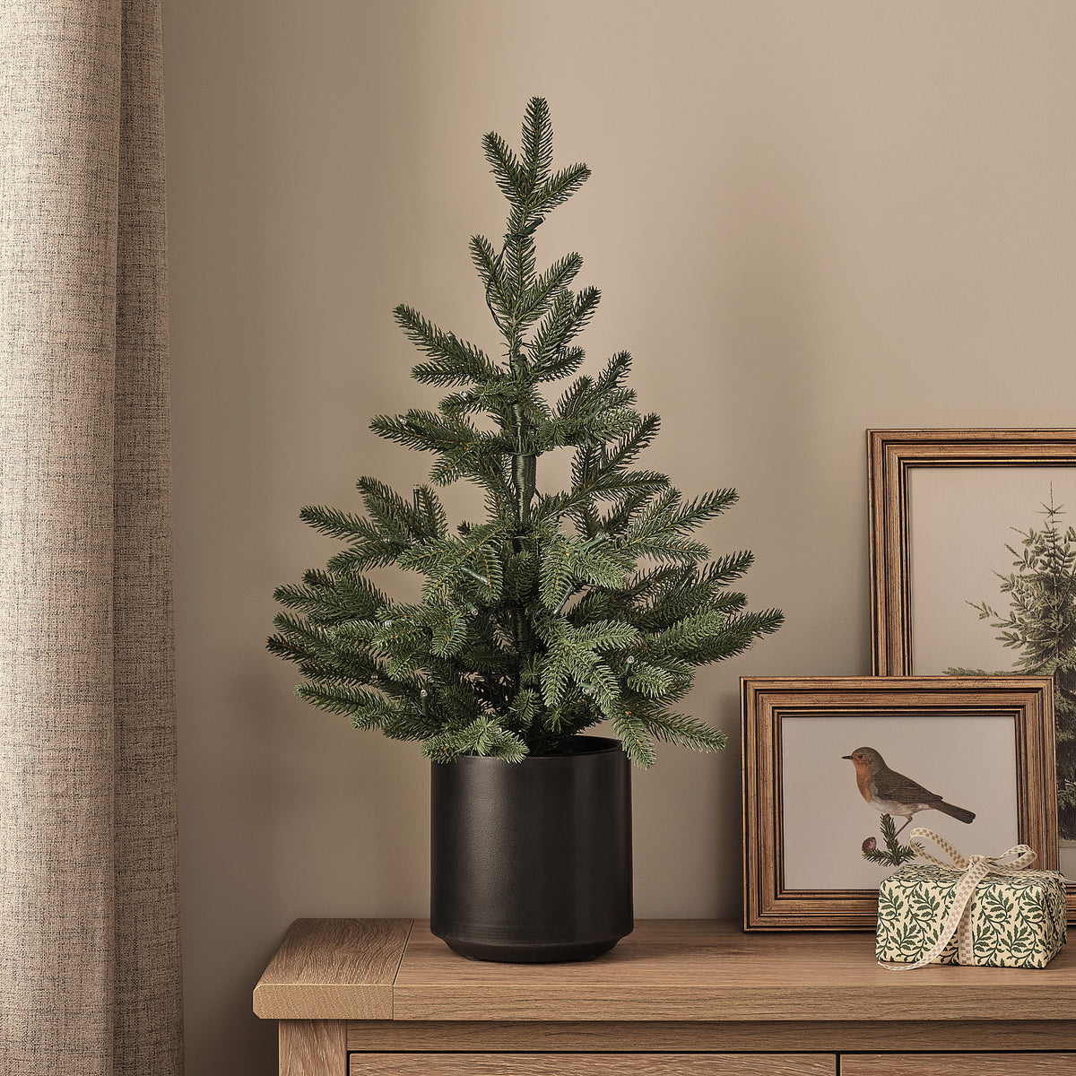 60cm künstlicher Fichten-Weihnachtsbaum im schwarzen Topf ohne Beleuchtung neben gerahmten Bildern