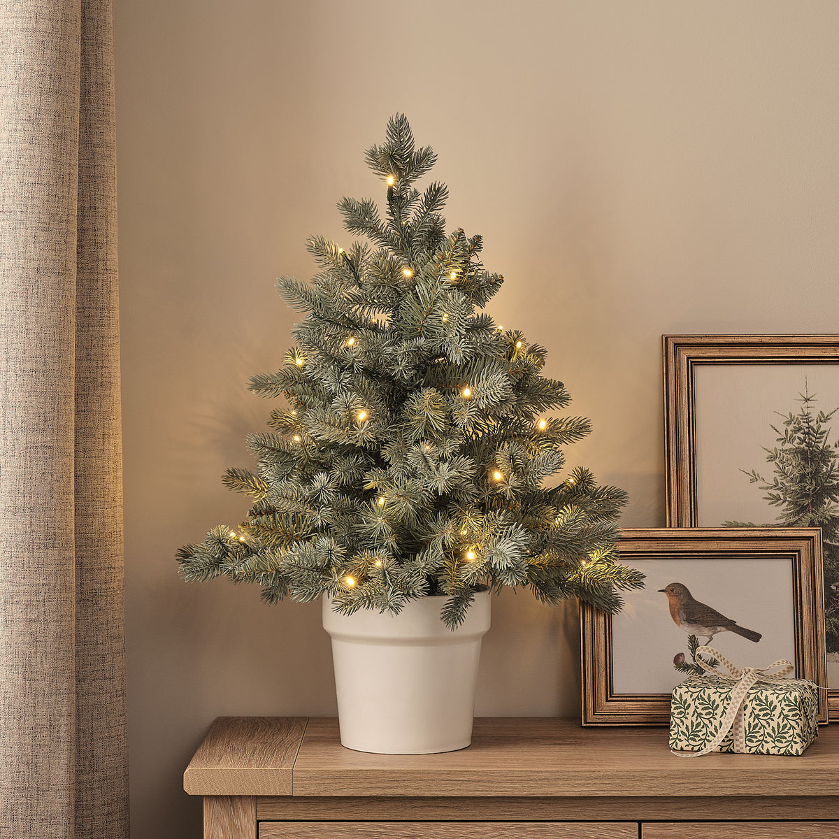 60cm künstlicher Douglasien-Weihnachtsbaum im weißen Topf mit warmweißen LED-Lichtern auf Holzkommode