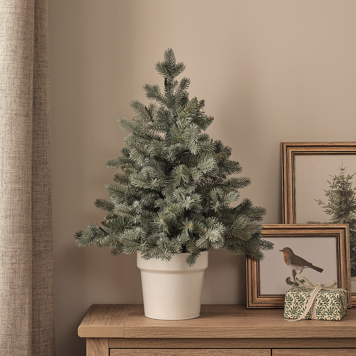 60cm künstlicher Douglasien-Weihnachtsbaum im weißen Topf ohne Beleuchtung auf Holzkommode neben Bilderrahmen