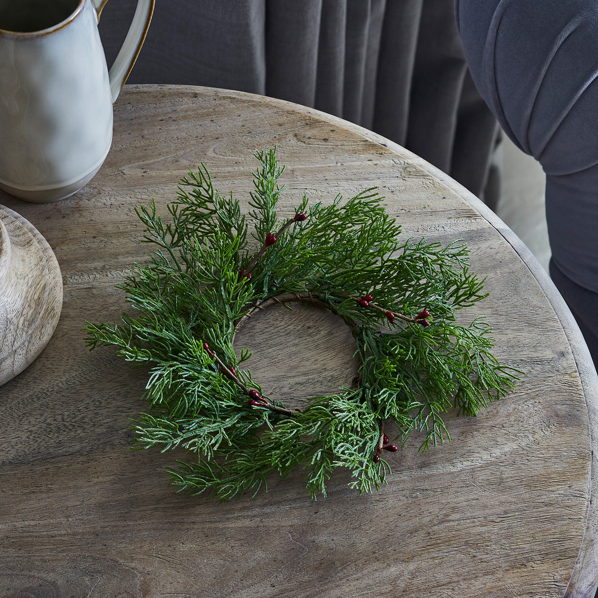 Weihnachtskranz mit roten Beeren und grünen Zweigen auf Holztisch vor grauem Hintergrund