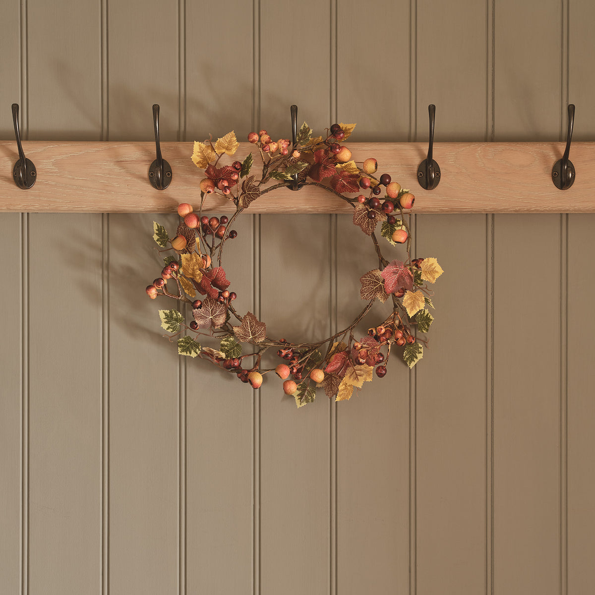 Herbstkranz mit Beeren und Ahornblättern an fünf Haken an Holzwand hängend