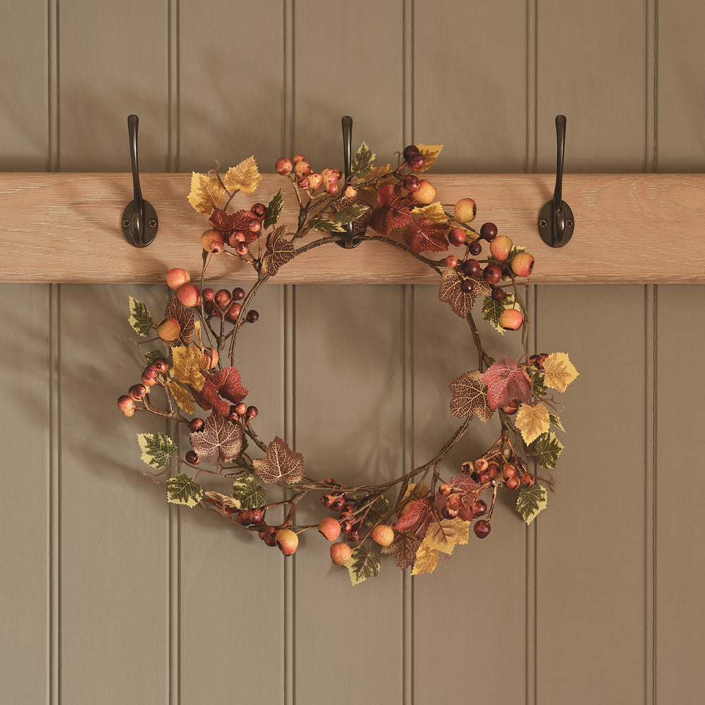 Herbstkranz mit Beeren und bunten Ahornblättern an drei Haken an Holzwand hängend