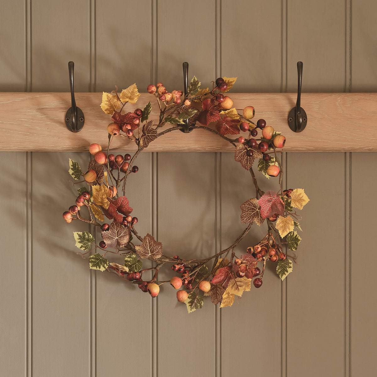 Herbstkranz mit Beeren und bunten Ahornblättern an drei Haken an Holzwand hängend
