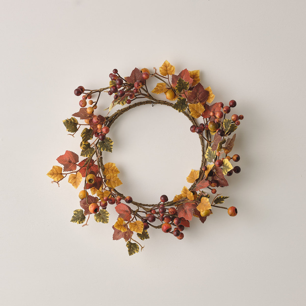 Herbstkranz mit Beeren und bunten Ahornblättern vor weißer Wand liegend