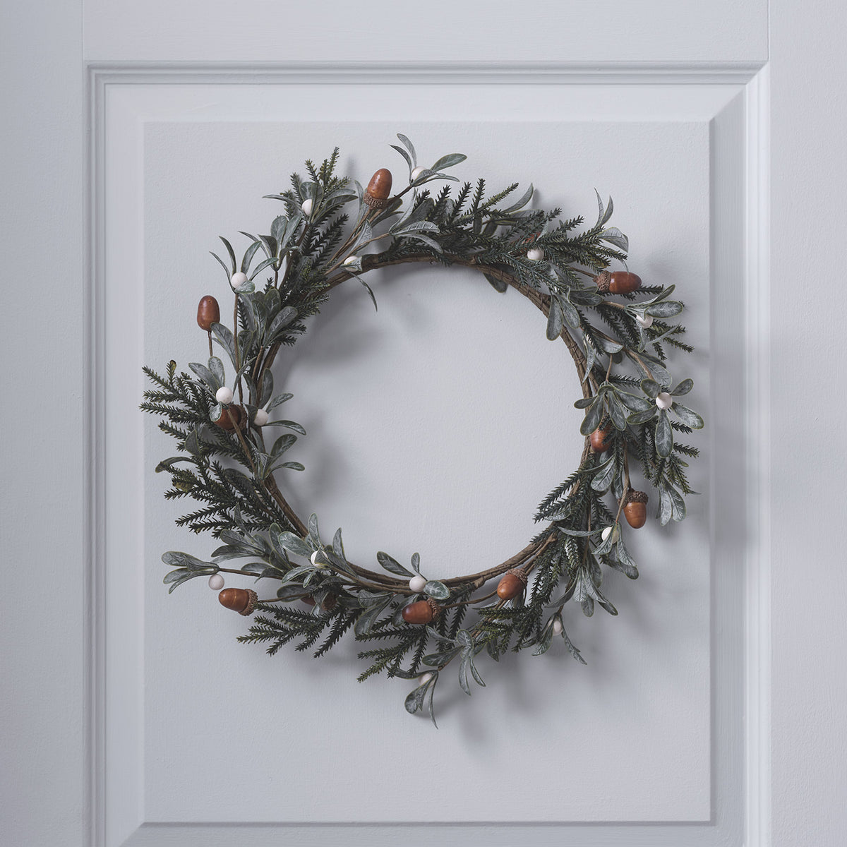 Weihnachtskranz mit Eicheln und weißen Beeren an weißer Tür hängend