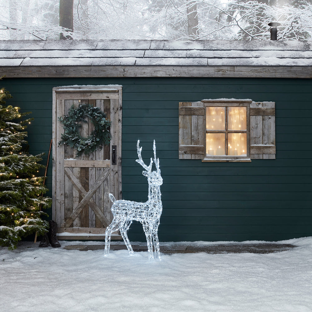 Solar-LED-Rentier vor grün gestrichener Holzwand mit Tür und Fenster im Schnee