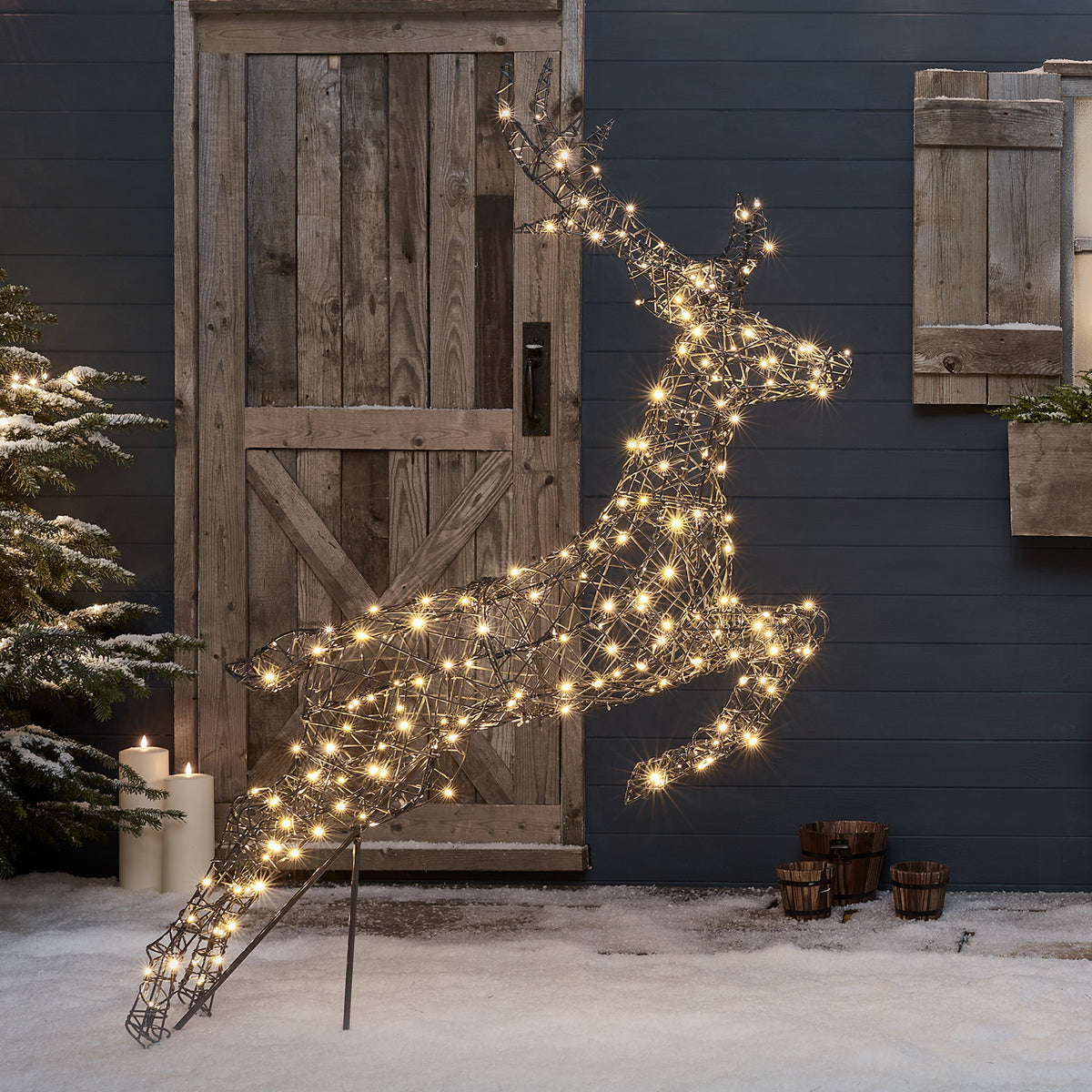 Springendes Rentier mit warmweißen LEDs vor Holztür und Schnee im Garten