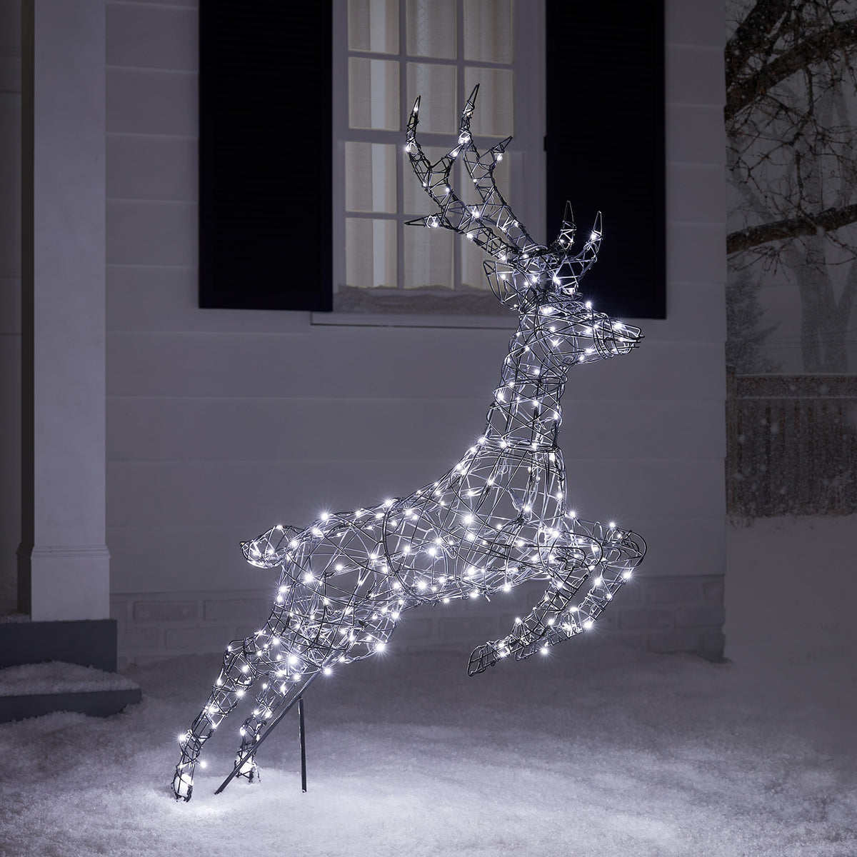 Springendes Rentier mit kühlen weißen LEDs beleuchtet auf verschneitem Boden vor Hauswand
