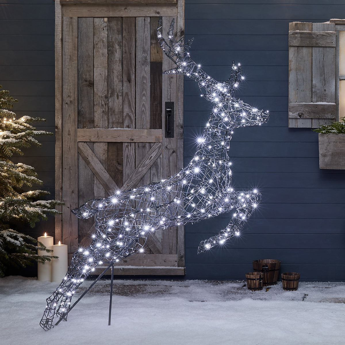 Springendes Rentier mit kühlen weißen LEDs vor Holztür und Schnee im Garten